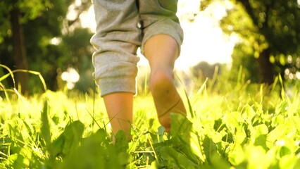 Enthusiastic son runs shoeless across lawn in meadow in summer time. Joyful son sprints barefoot...