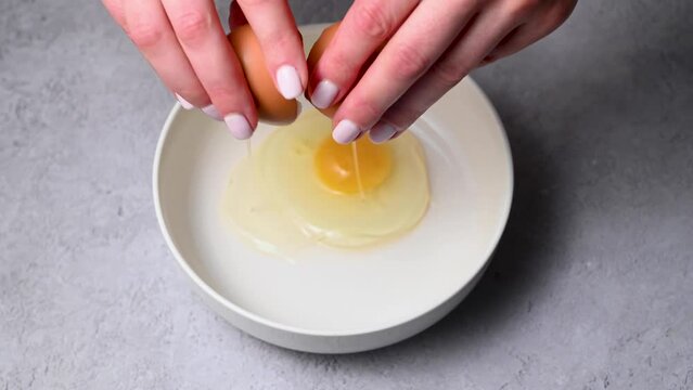 Female hands holding a cracked egg and breaking it. Cooking breakfast or baking. Protein food