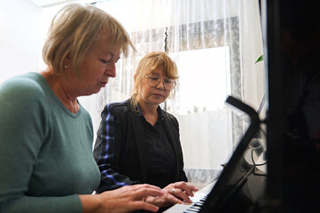 A mature Caucasian woman teaches her friend to play the piano. Music lesson