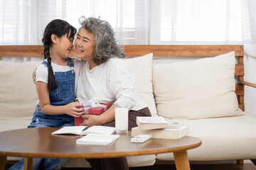 Asian girl giving her grandmother a present box and kissing cheek. Granddaughter visit senior woman on holidays weekend. Family meeting, bonding relationship. Healthy living insurance after retired