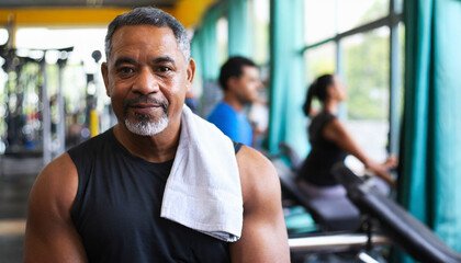 Fototapeta na wymiar Portrait of smiling senior man with towel on shoulders in fitness center