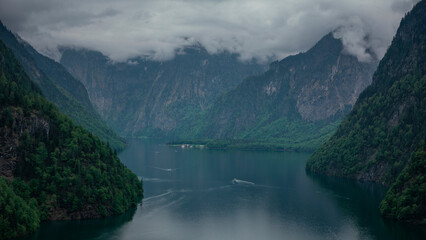 View to lake Königssee from above during moody weather, tourist boats on the water, mountains in...