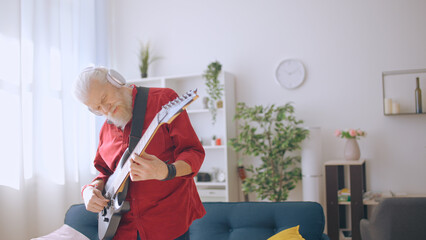 Trendy mature man with gray hair plays the electric guitar, mastering a new chord