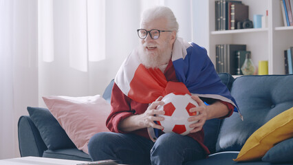 A happy grandpa celebrates the victory of the French football team, showing his joy as a supporter