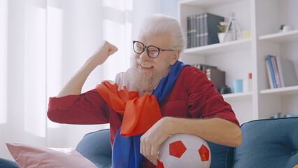 A positive man in his 60s, draped in the French flag, cheers for a sports team, indulging in his...