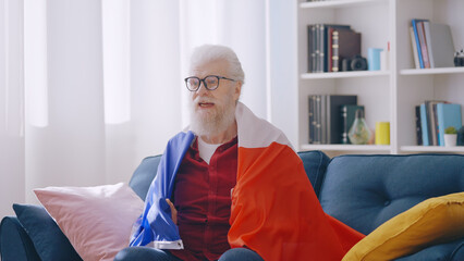 A concentrated mature man with a French flag on his shoulders cheers for his team in a competition
