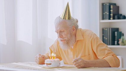 A senior man blows out candles on his birthday cake, marking his special day during the coronavirus...