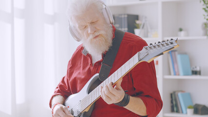 A concentrated mature man in headphones immerses himself in playing the electric guitar at home,...