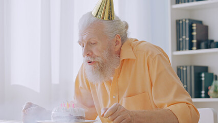 A grandpa makes a wish and blows out candles on his birthday cake, celebrating alone