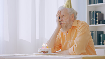 A disappointed senior man celebrates his birthday alone at home, feeling a sense of sadness and...
