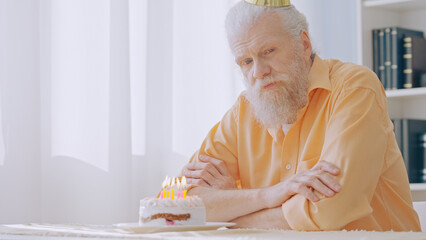 An upset grandpa wears a party hat, marking his birthday alone, embodying a lonely senior man