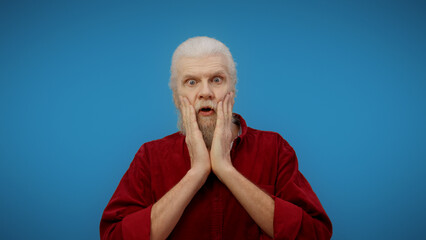 Portrait of a surprised and shocked senior man against a blue background, a picture of pure...