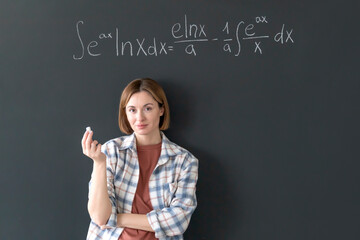 A young female student writes a complex mathematical formula on the blackboard	