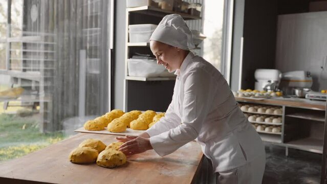 Female baker prepares raw bun before baking in oven