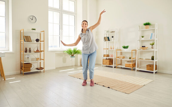 Full body photo of young happy smiling girl wearing casual clothes dancing in the living room at home. Beautiful woman having fun with a satisfied face expression. People emotions concept.