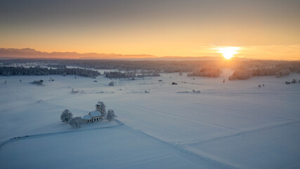 Bavarian church of Raisting with trees and snow during winter and sunset from above, snow field in the foreground, Bavaria Germany. - 702369373