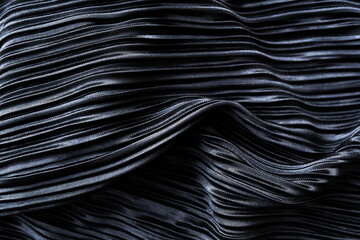 Naklejka premium A close-up view of a dark-colored fabric with intricate wavy patterns. The fabric has a glossy finish that reflects light and emphasizes the richness of its color and texture.