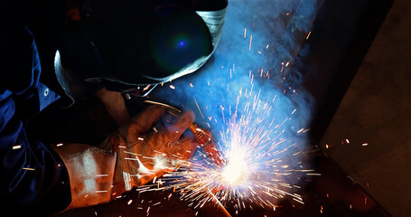 Welder at work in metal industry, welding metal construction. Close-up shot lots of sparks in the factory