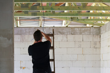 Unrecognizable man standing on a ladder, view from behind - electrician - installing cables at...