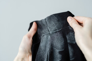 Fototapeta premium Deodorant stains on black clothes. Women's hands holding spoiled clothes. daily life stain concept. 