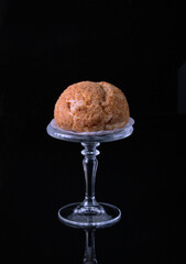 Shu cake on a glass pedestal, on a black background, copy space
