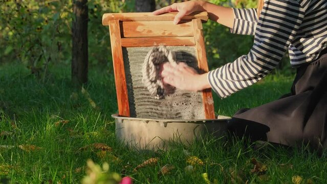 Close-up of a woman's hands washing clothes on old vintage washboard outdoors in summer day. Antique Washboard. Woman washing on a retro washboard. Washerwoman doing laundry by hand