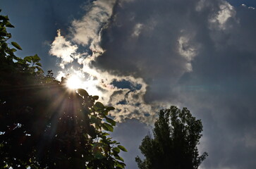 Background of rainy fluffy clouds floating in a blue sky with a bright sun shining between them, Sofia, Bulgaria 