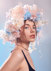 portrait of a beautiful woman in a flower wreath looking at the camera on a blue background