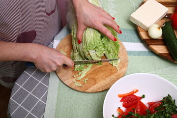 Woman cutting fresh beijing cabbage in kitchen