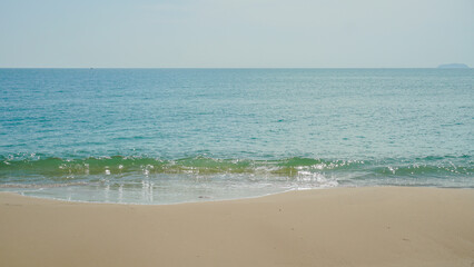 White sand beach and blue sky. Blue and aquamarine color sea waves and yellow sand with white foam. Marine beach background.