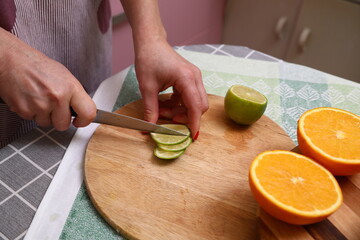 Hand Holding Knife Cut Lime on Chopping Board in Kitchen.