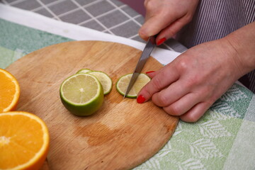 Hand Holding Knife Cut Lime on Chopping Board in Kitchen.