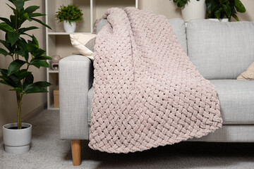 Knitted large plaid blanket in dusty rose light grayish-red color on the sofa.