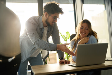 Young caucasian businessman showing something on laptop to his female colleague