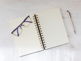 Spiral notebook open flat lay mockup with reading glasses and pen on wooden background Top view. - 702410991