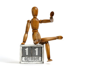 October 11, wooden calendar with mannequin sitting on it on white background. Calendar date.