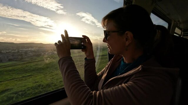 Female traveling by train, admiring beautiful view and taking pics with phone. Young tourist lady is on a train ride across picturesque England. She uses public transportation to explore the country.