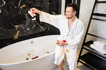 Smiling male preparing a bath with rose petals