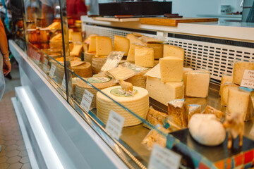 Delicatessen shop with various cheese in the display cabinet and a worker behind the counter at...
