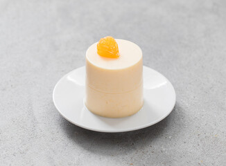 Tangerine Panna Cotta of cylindrical shape. On a plate. Light grey background. Close-up
