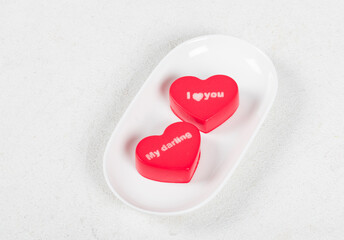 Valentine's Day. Couple. Two Strawberry chocolate cream mousse cakes in the shape of a red heart with white thematic inscriptions on top "I love you", "My darling". On a serving plate.