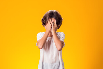 Kid girl feeling fear, closed her eyes with hands over yellow background. Frustration concept