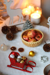 Cup of tea or coffee, glass of wine or juice, bowl of cookies, organic pomegranate, fluffy blanket, pine cones, various Christmas decorations and lit candles on the table. Christmas hygge concept.