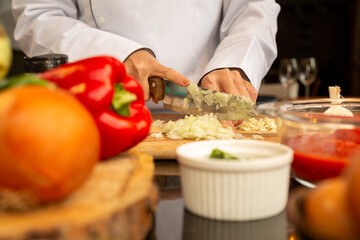 mão de chef picando alho e cebelo e preparando legumes para receita na cozinha