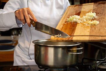 Chef de cozinha com dólmã branco segurando tábua de corte em uma mão e na outra um facão inox,...