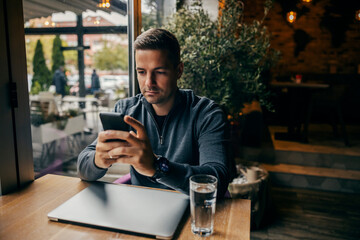 A man sitting in coffee shop and using his phone. - obrazy, fototapety, plakaty