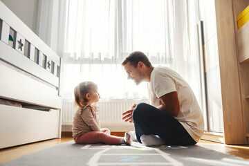 An angry toddler is sitting in nursery room with father. Dad is teaching a girl good manners. - obrazy, fototapety, plakaty