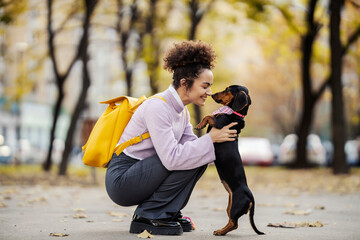 A young trendy woman is cuddling with her dog on a city street.