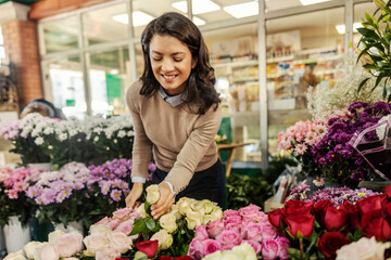 A cheerful woman is choosing roses and flowers at farmers market.