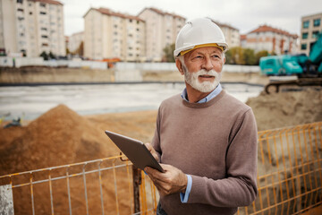 A senior architect is visiting construction site and using tablet.